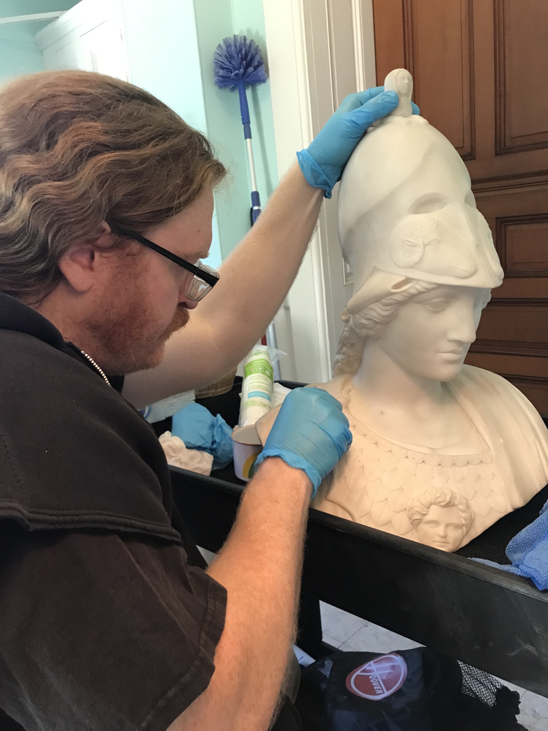 Volunteer Ryan Lance cleans the stature of Minerva from the Reception room with distilled water and cotton swabs.