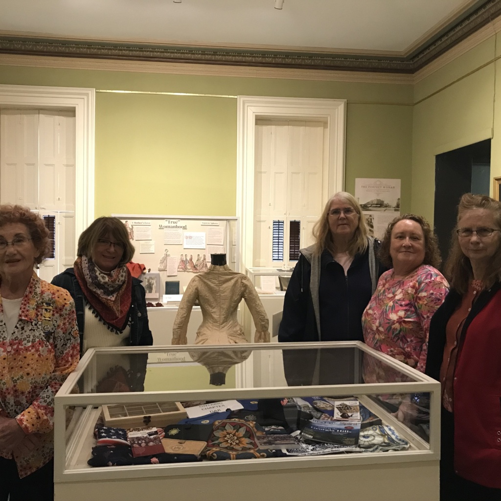 Daughters of the Revolution Betsey Baldwin Chapter stand around a display case in the museum's temporary gallery.