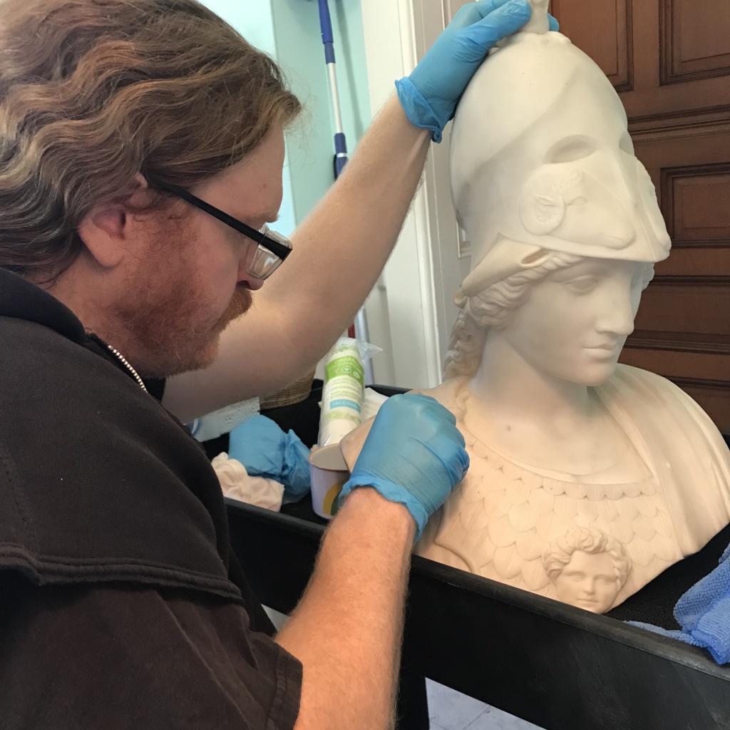 Volunteer Ryan Lance cleans the stature of Minerva from the Reception room with distilled water and cotton swabs.
